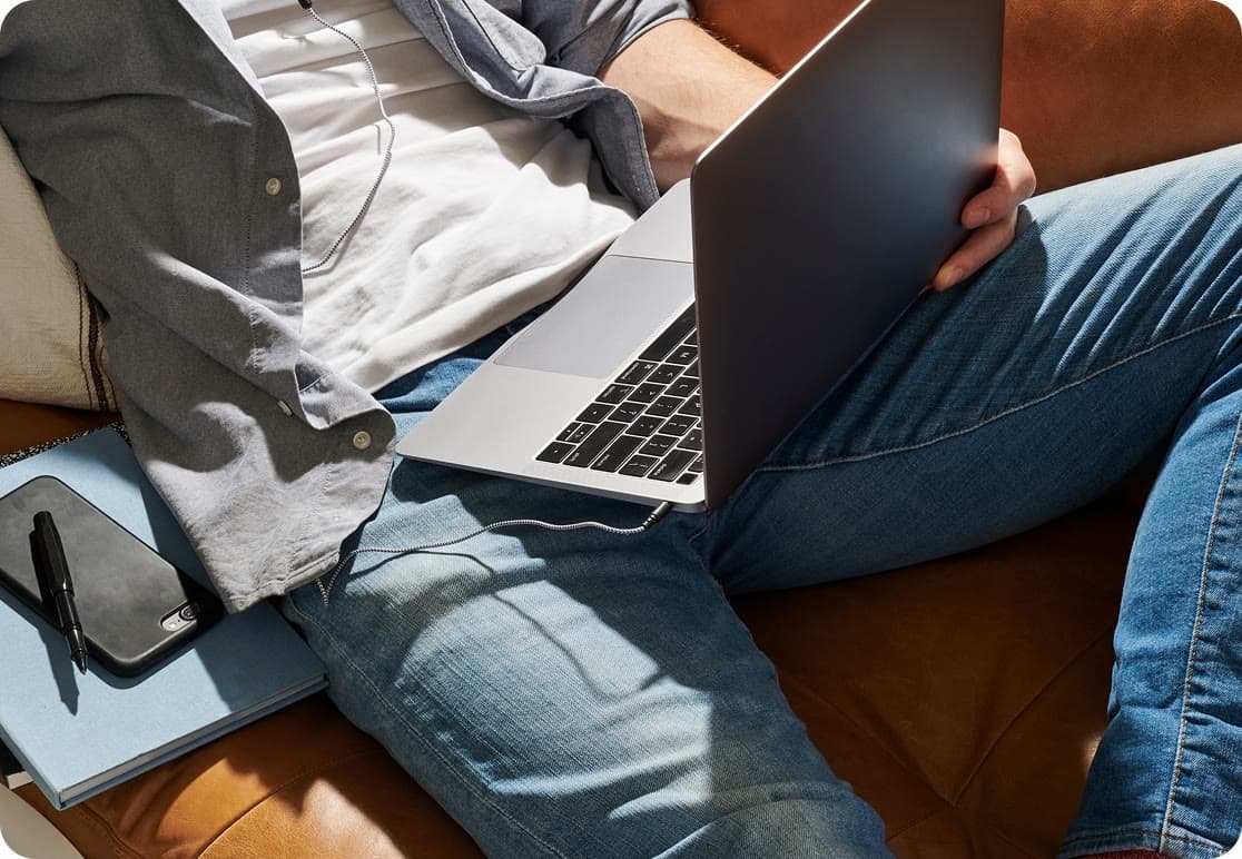 Someone sitting on a couch with a laptop resting on their knee